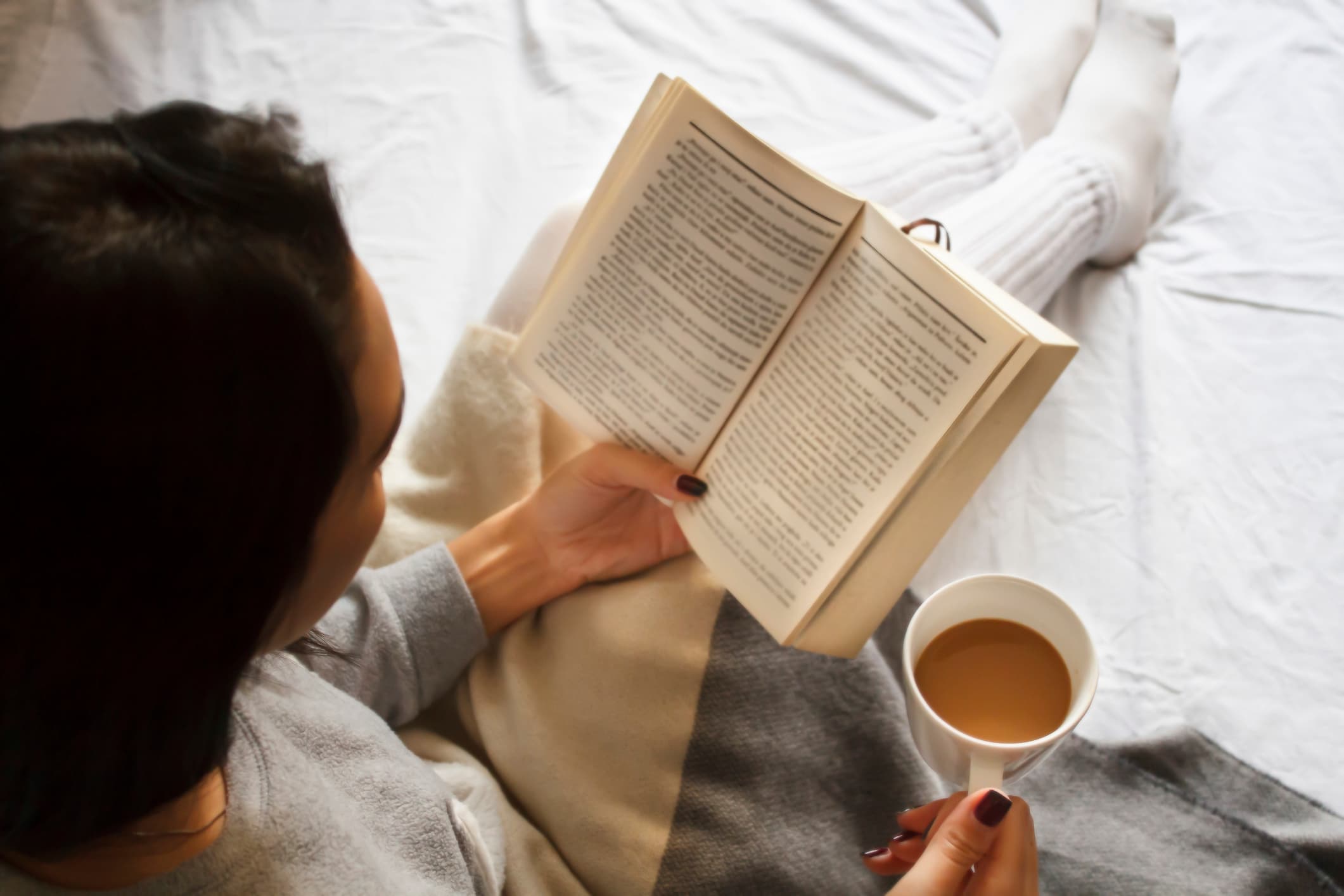 woman reading a book and holding a mug of coffee