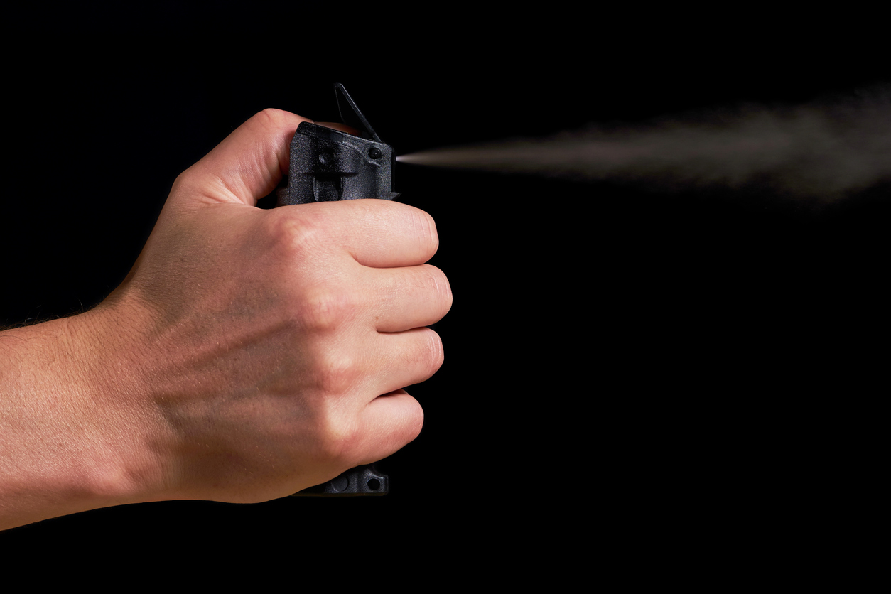 man aiming and spraying pepper spray with visible fog on black background